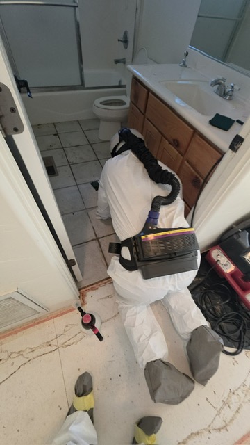 Technician decontaminating a biohazard floor with powered respirator